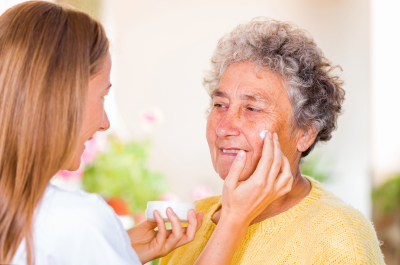 caregiver rubs the face cream on the elderly womans face